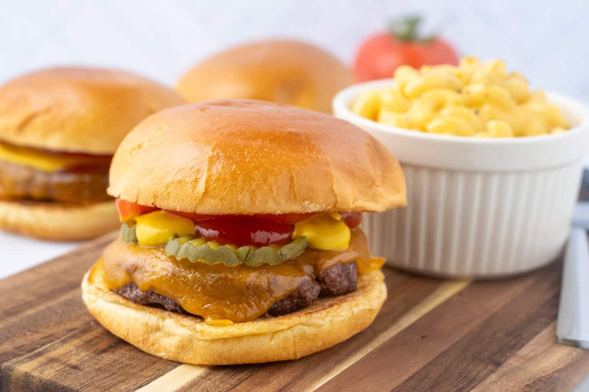 Baked hamburger patty with cheese on a bun with pickles ketchup and mustard with a side of macaroni and cheese