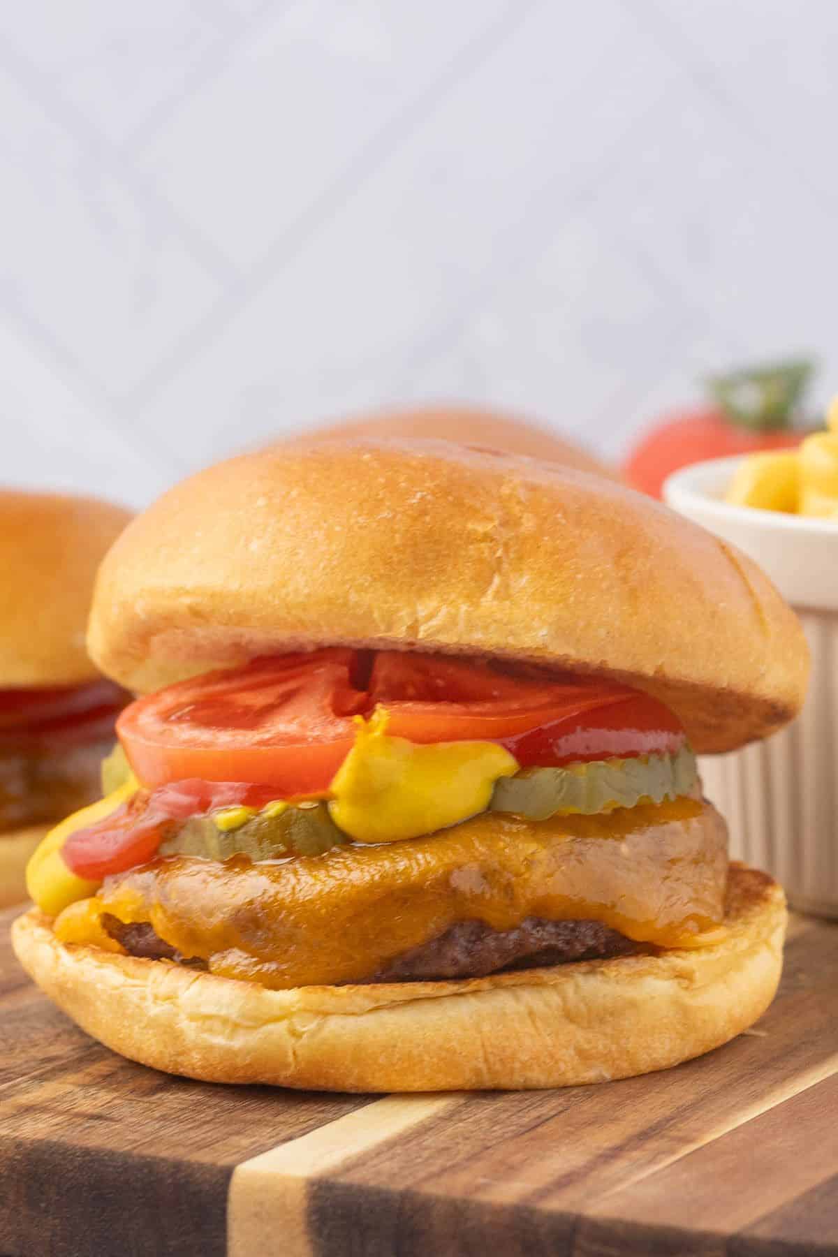 baked burgers with all the fixings on a wooden surface, with one in focus and others in the background.