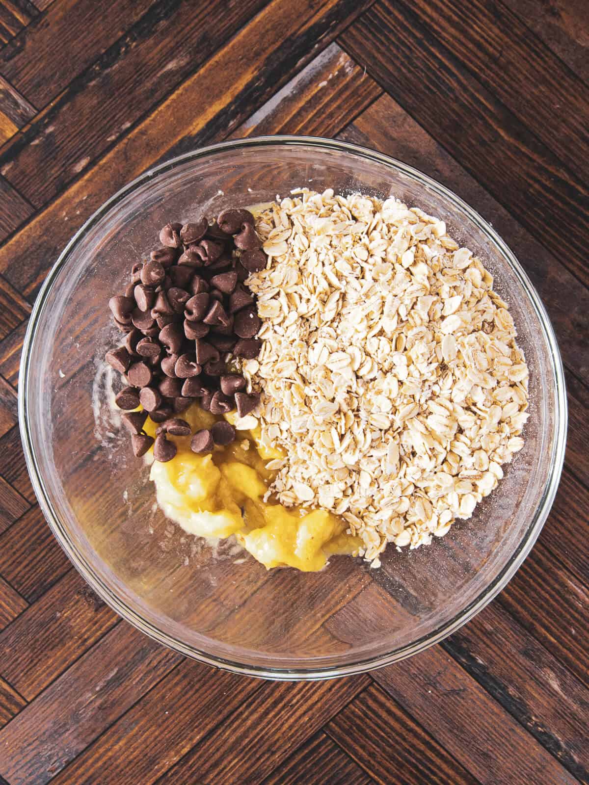 A bowl containing mashed bananas, oats, and chocolate chips before mixing.