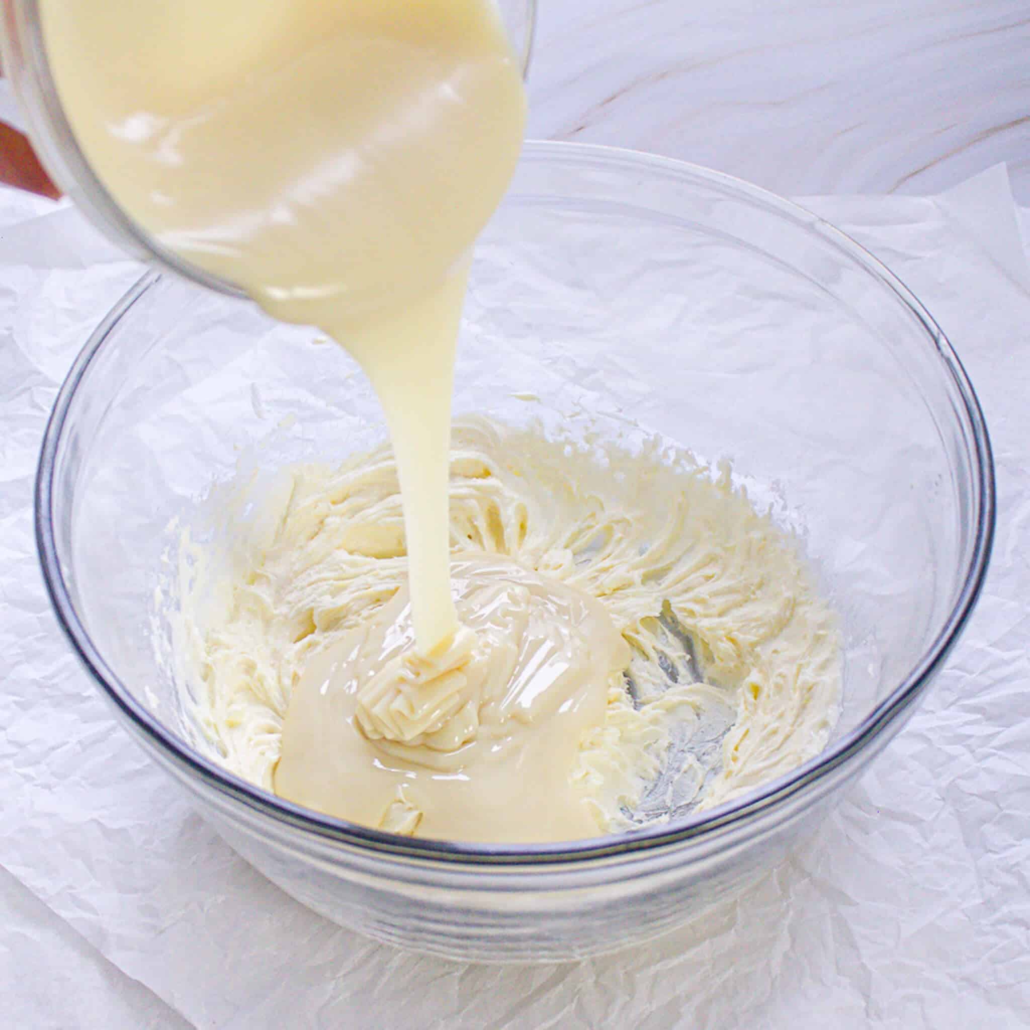 A thick, creamy mixture being poured into a bowl of whipped ingredients.