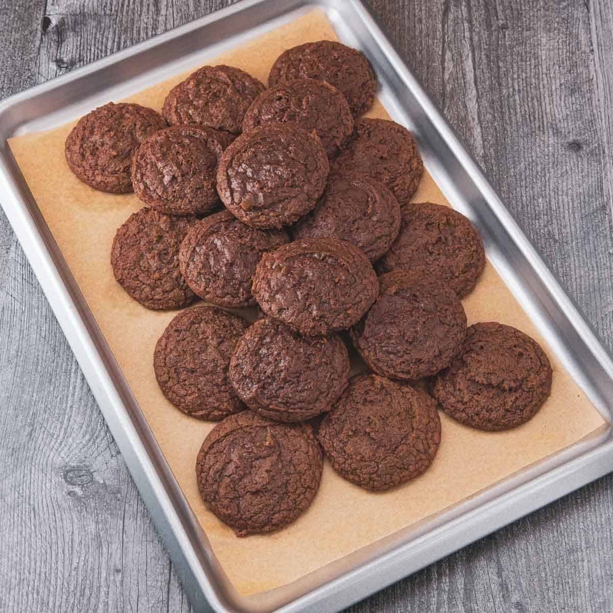 A tray full of freshly baked chocolate brownie cookies cooling on parchment paper.