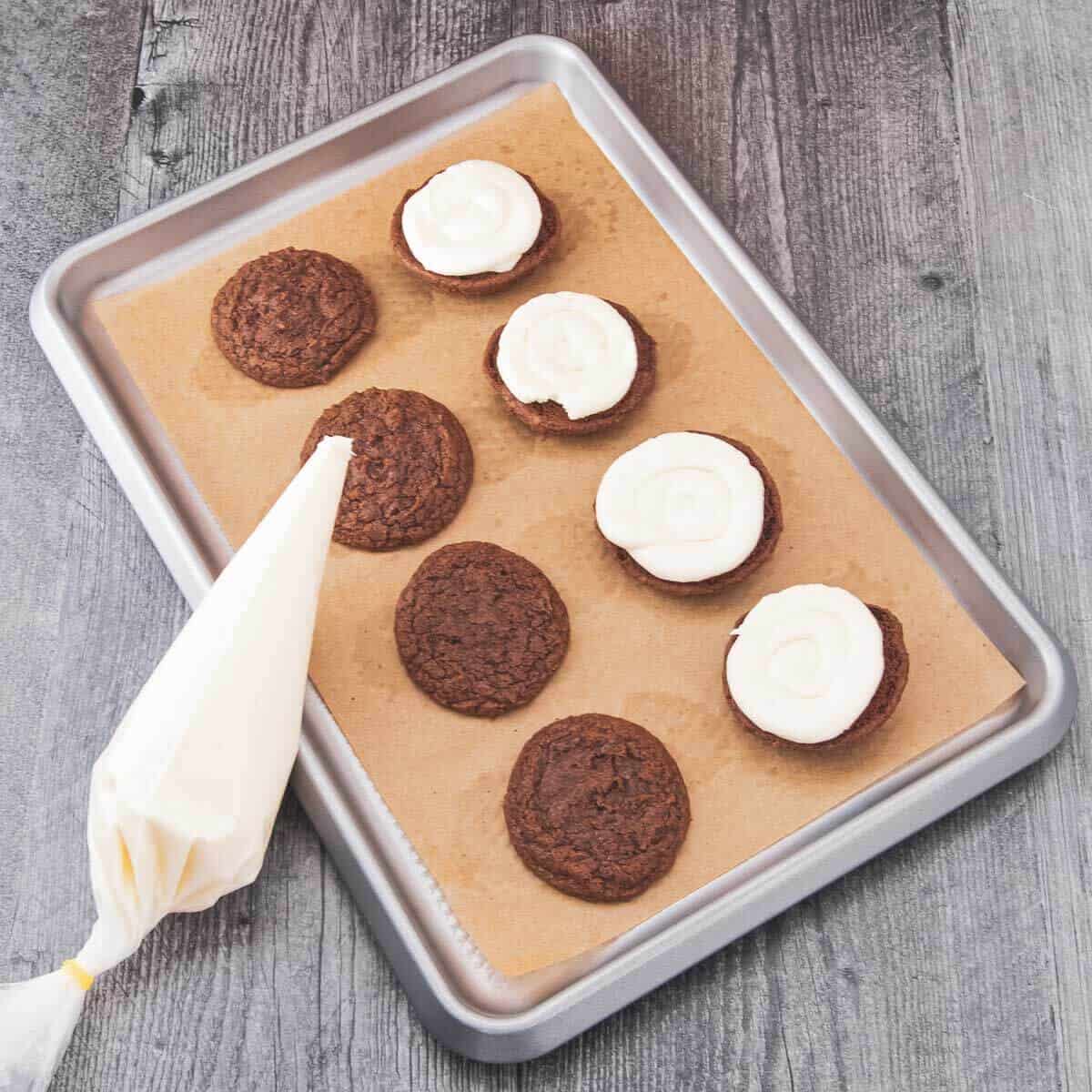 A piping bag is used to swirl cream cheese filling onto half of the cookies