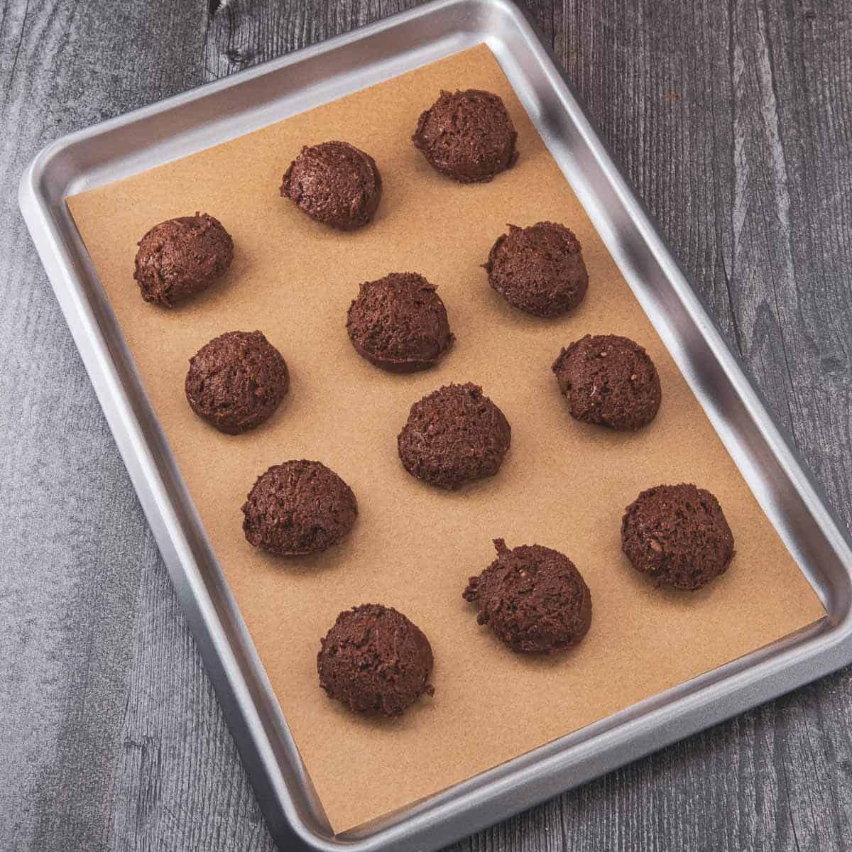 Small mounds of brownie cookie dough placed on a parchment-lined baking sheet, ready to bake.