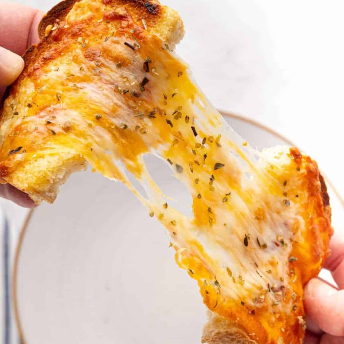 Cheese toast being pulled in half to show how cheesy it is and melty
