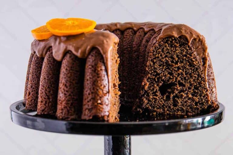 chocolate orange cake with chocolate ganache and orange slices on top, with a slice removed to reveal the moist interior, all on a black cake stand