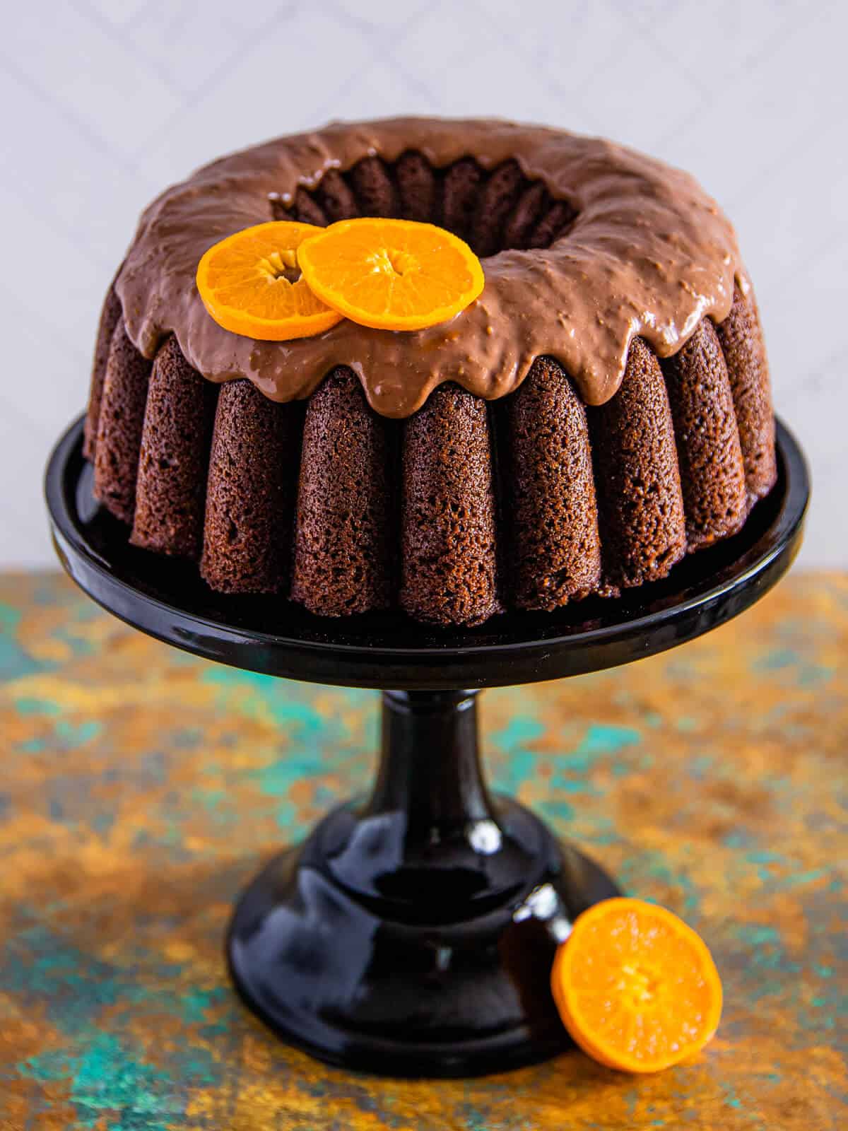 A beautifully presented chocolate orange bundt cake on a black cake stand, topped with chocolate glaze and orange slices.