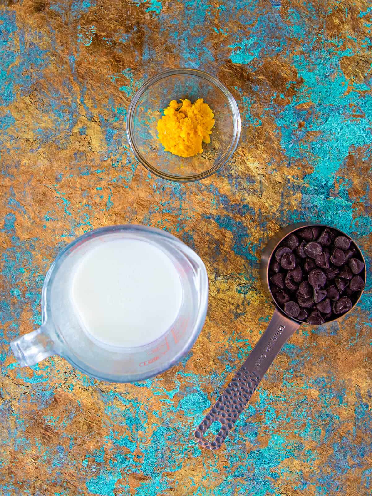 A display of chocolate chips, heavy cream, and orange zest on a colorful textured surface, prepped for making ganache.