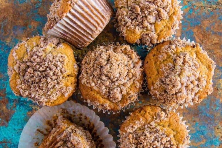 Overhead view of several cinnamon streusel muffins arranged on a rustic blue and brown surface