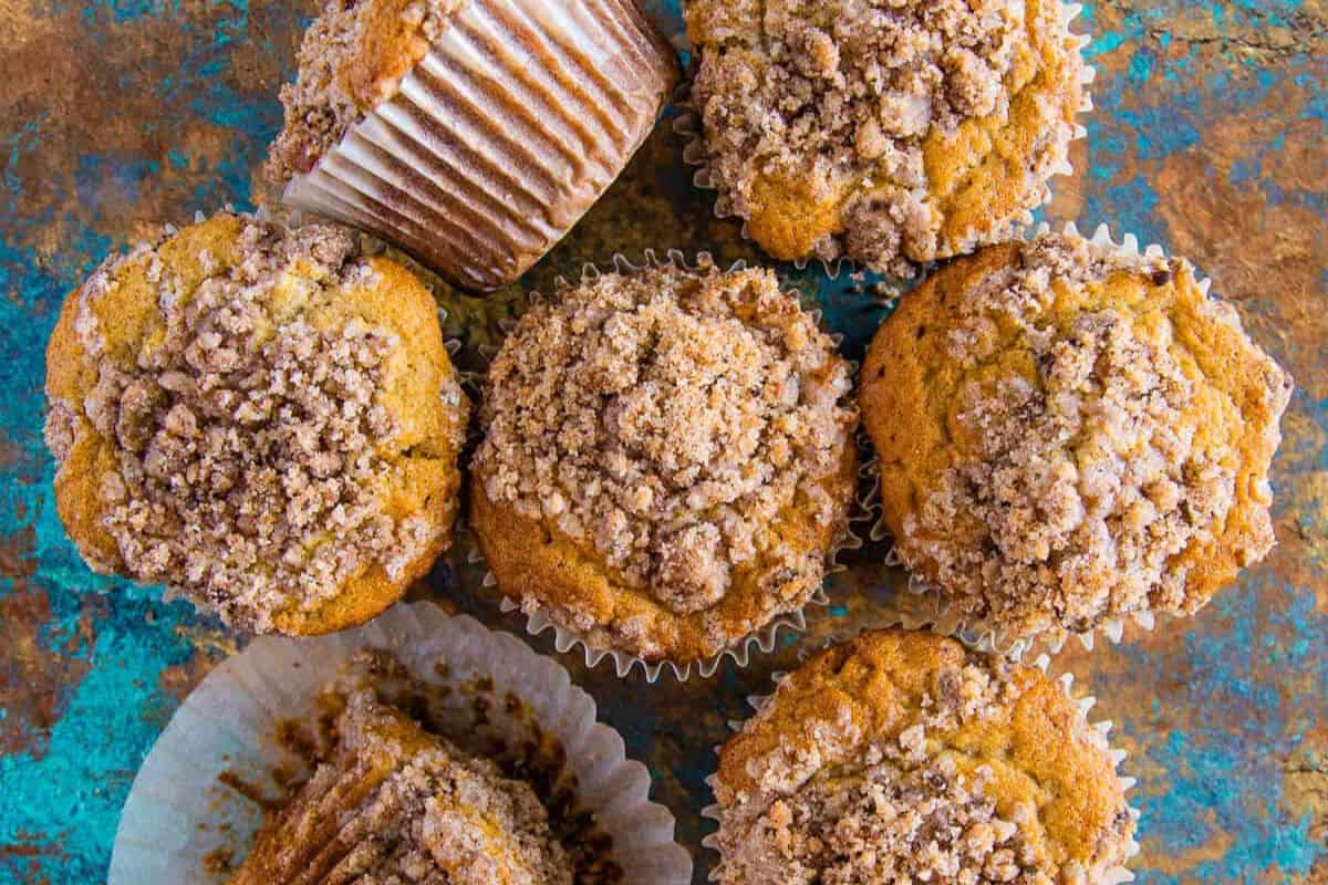 Overhead view of several cinnamon streusel muffins arranged on a rustic blue and brown surface