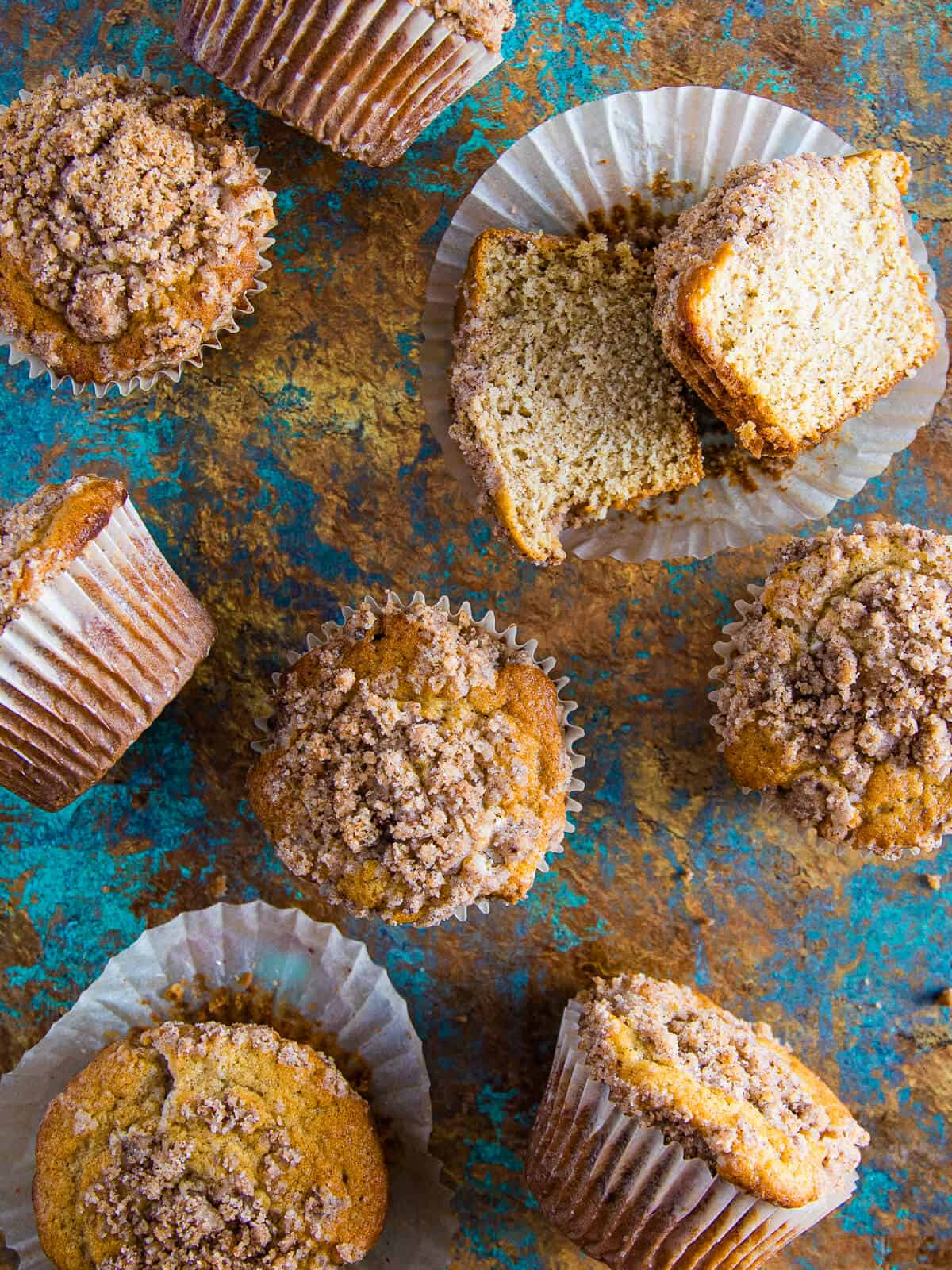 Multiple cinnamon streusel muffins arranged on a rustic background, with one sliced open