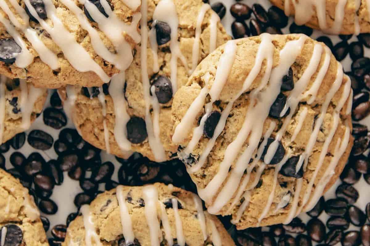 Close up view of several coffee cookies with white icing drizzle, surrounded by roasted coffee beans