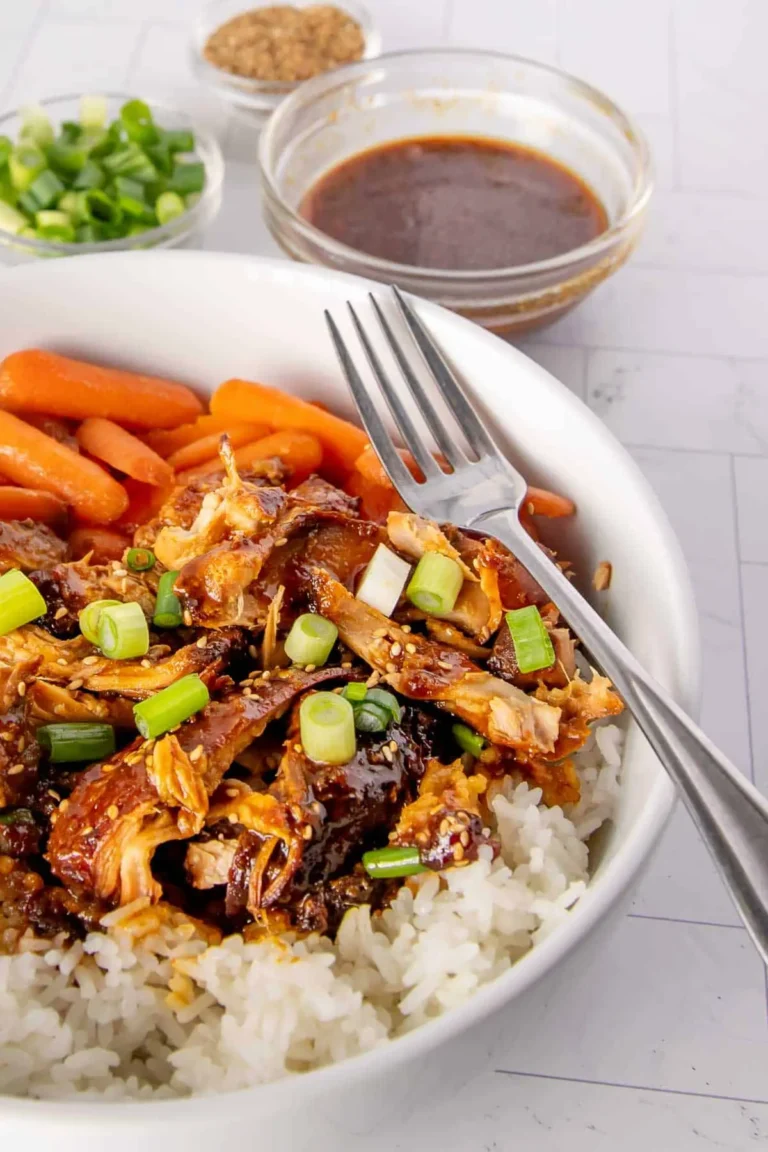 Crockpot apricot chicken thighs shredded on top of a bed of rice with carrots and garnished with green onions.
