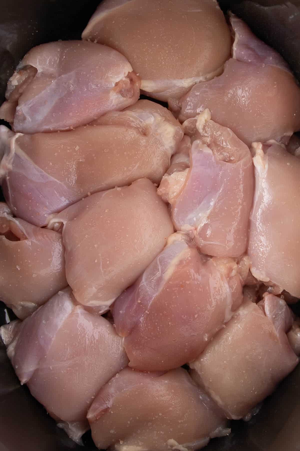 Uncooked chicken thighs arranged in the base of a slow cooker