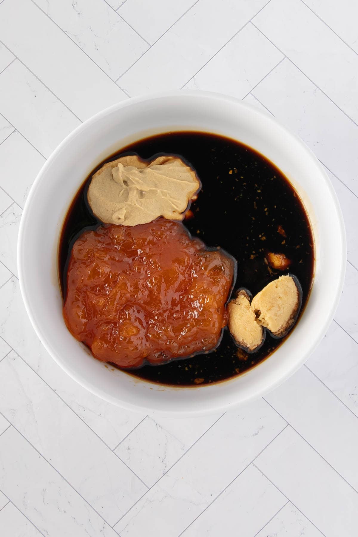 Apricot preserves, soy sauce, mustard, garlic, and ginger in a white mixing bowl before whisking