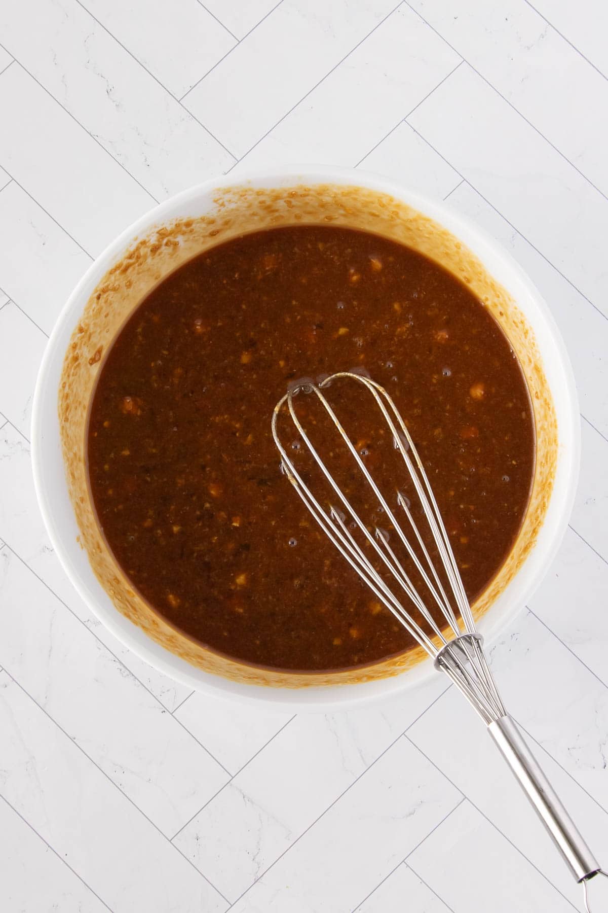 A bowl of dark apricot sauce fully whisked and ready to pour, with a metal whisk resting in it