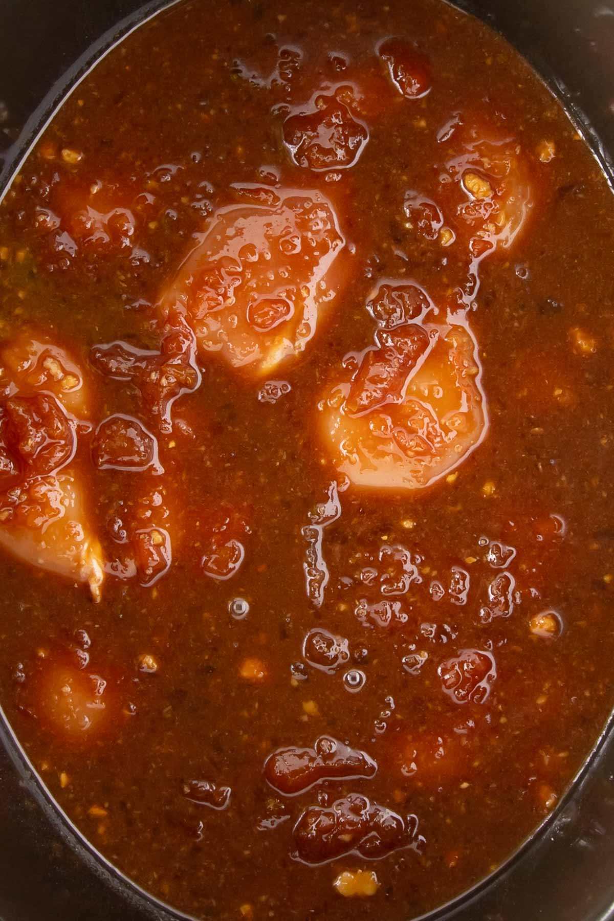 Raw chicken thighs in a slow cooker, now covered with the mixed apricot sauce