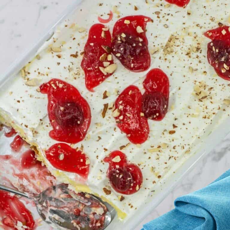 heaven on earth cake topped with cherry pie filling and nuts in a white container next to a blue napkin