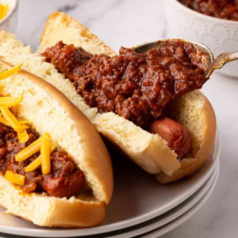 hot dog chili being spooned onto a hot dog inside a bun on a plate with a spoon
