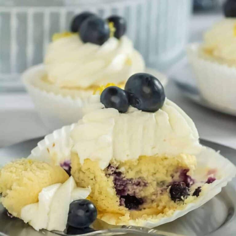 blueberry lemon cupcake with a portion missing showing the blueberries inside the cupcake with the frosting on top