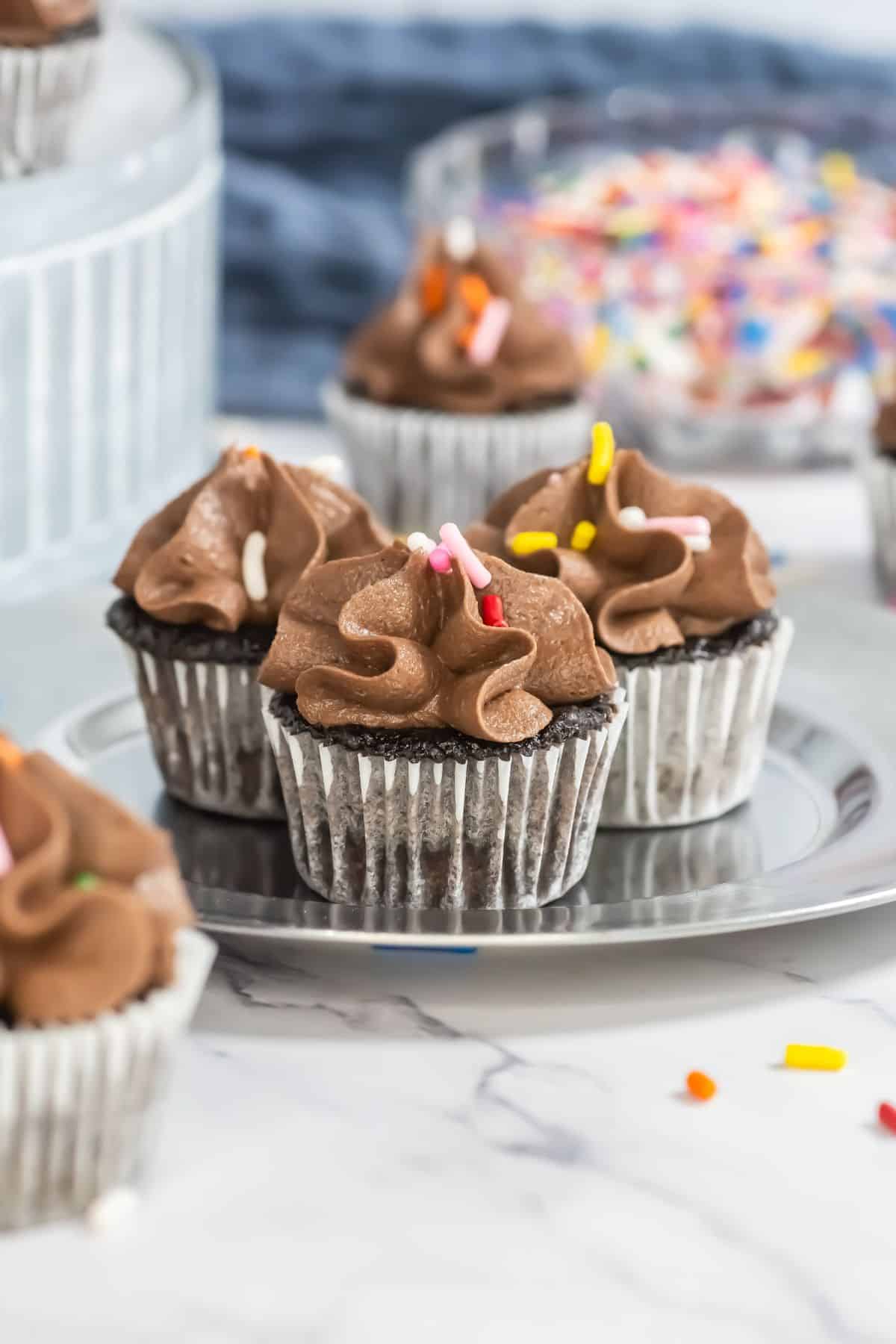 small silver plate with 3 mini chocolate cupcakes with chocolate frosting and sprinkles