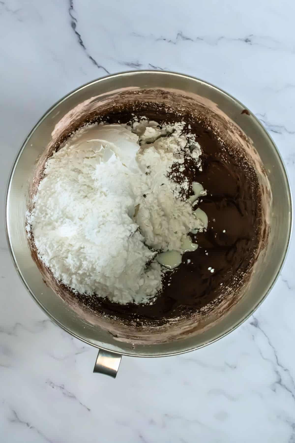 stand mixer bowl with chocolate frosting half made with second cup of powdered sugar on top
