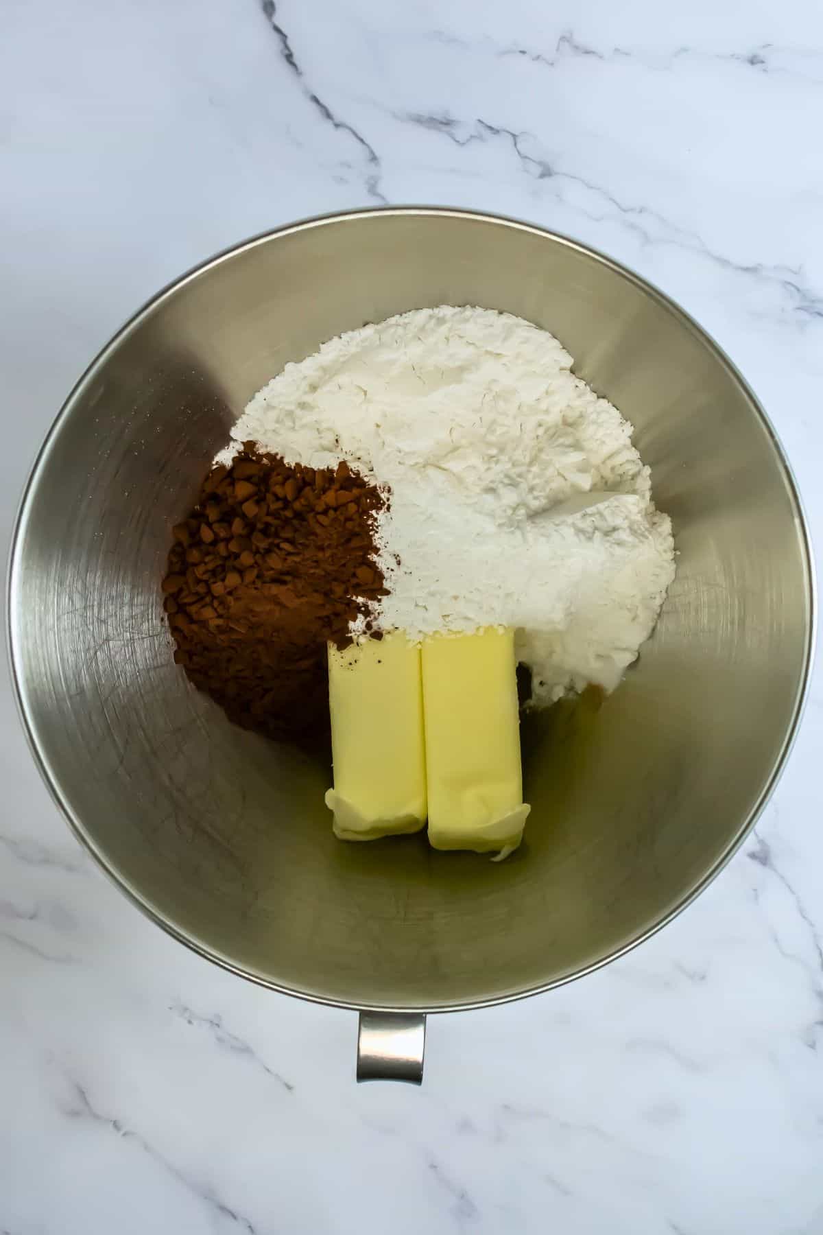 stand mixer bowl with ingredients for chocolate frosting butter, powder sugar and cocoa powder