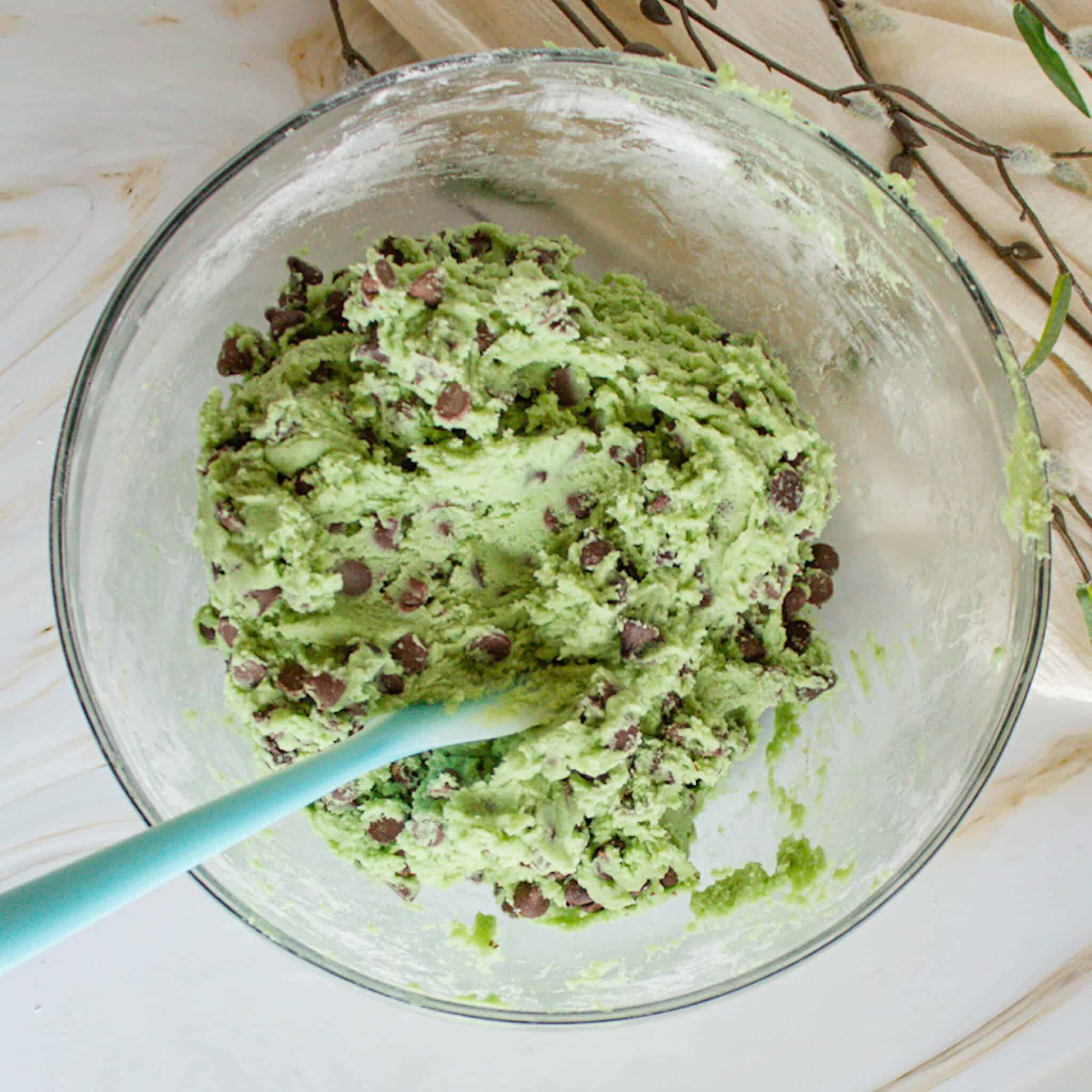 A bowl of vibrant green mint chocolate chip cookie dough with chocolate chips mixed in.
