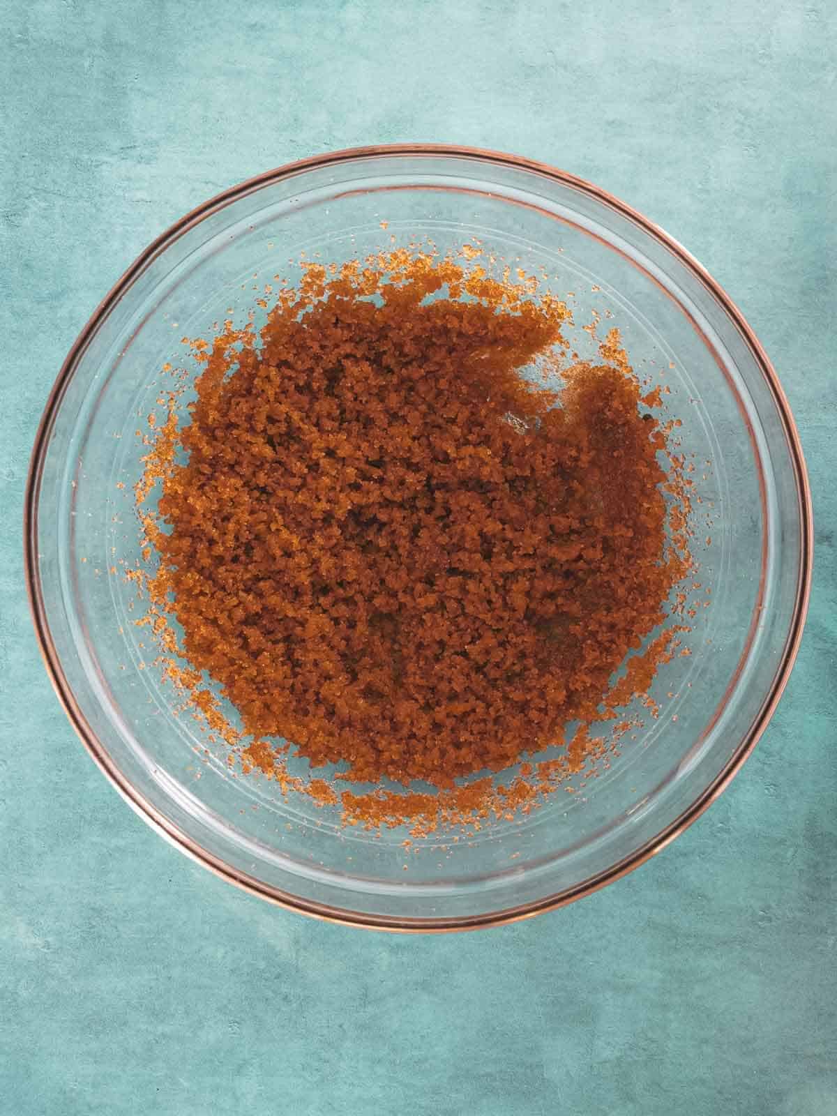 A glass bowl with brown sugar on a turquoise background.