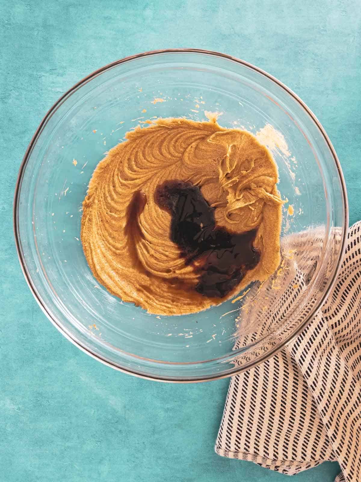 A bowl of creamed butter and sugar with molasses being added.