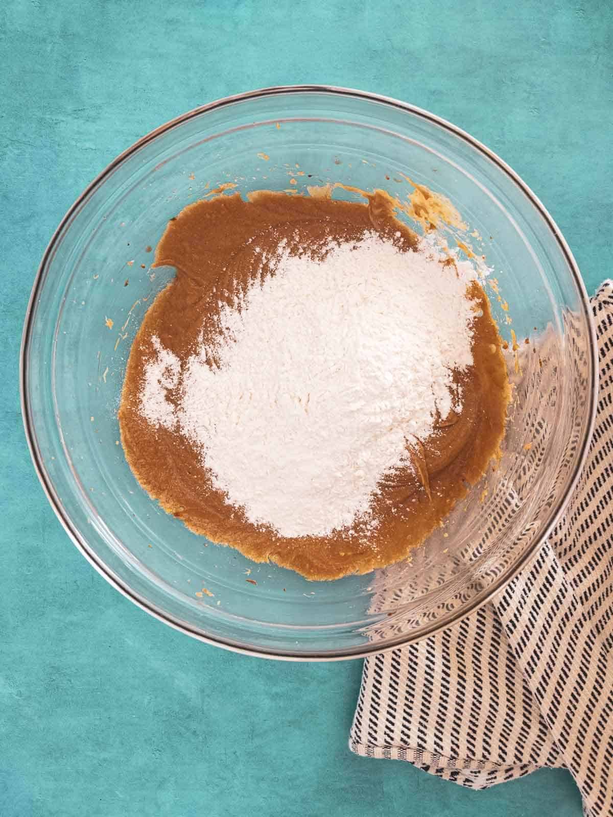 A bowl with cookie dough and a mound of flour on top.