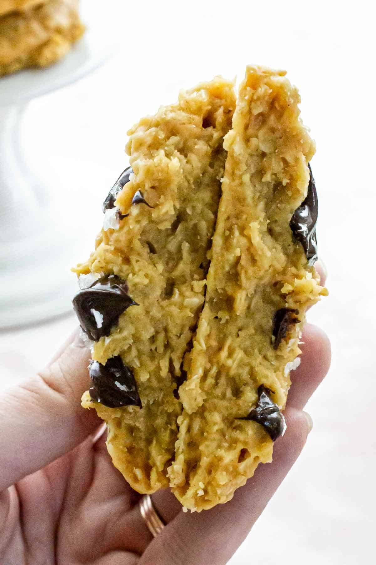 A hand holding a broken cookie, showing its soft and chewy interior with melted chocolate.