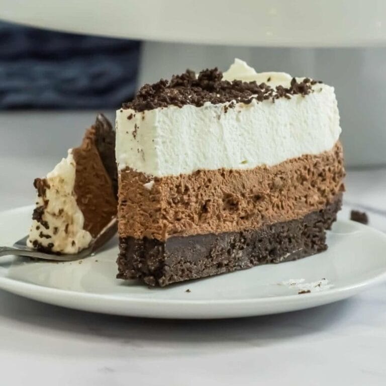 a slice of no bake oreo dessert on a plate with three visable layers an oreo crust bottom chocolate mousse center and whipped cream on top