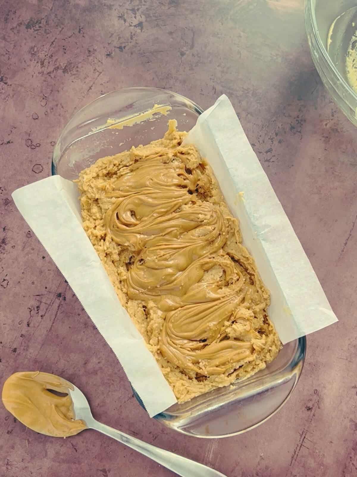 A parchment-lined loaf pan with peanut butter batter and a decorative swirl of peanut butter on top.