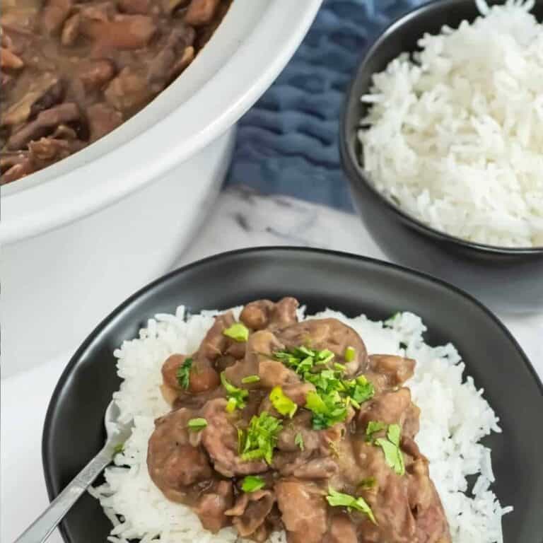 A plate of slow cooker red beans and rice in the center. A crock pot in left corner with red beans and sausage, bowl of white rice in the right corner