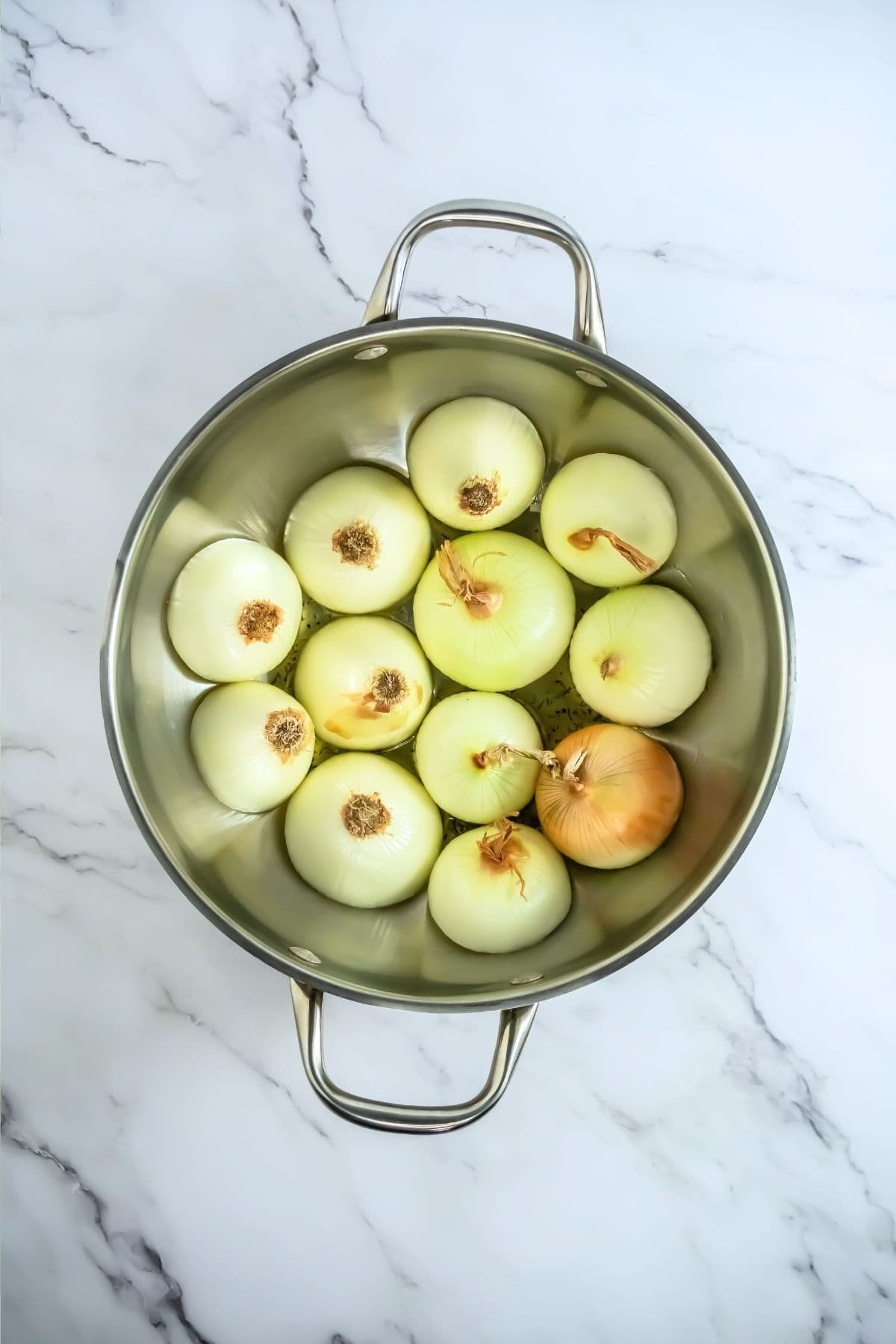 onions cut in half with the cut side down in an oven safe pan for roasting.