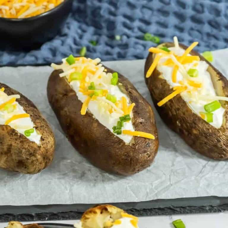 slow cooker baked potatoes 3 of them on a black plate topped with sour cream and cheese and green onions