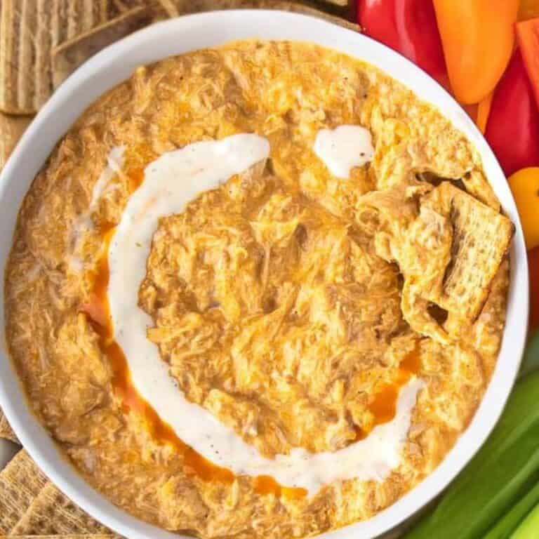 Crock pot buffalo chicken dip in a while bowl with crackers and veggies around the sides