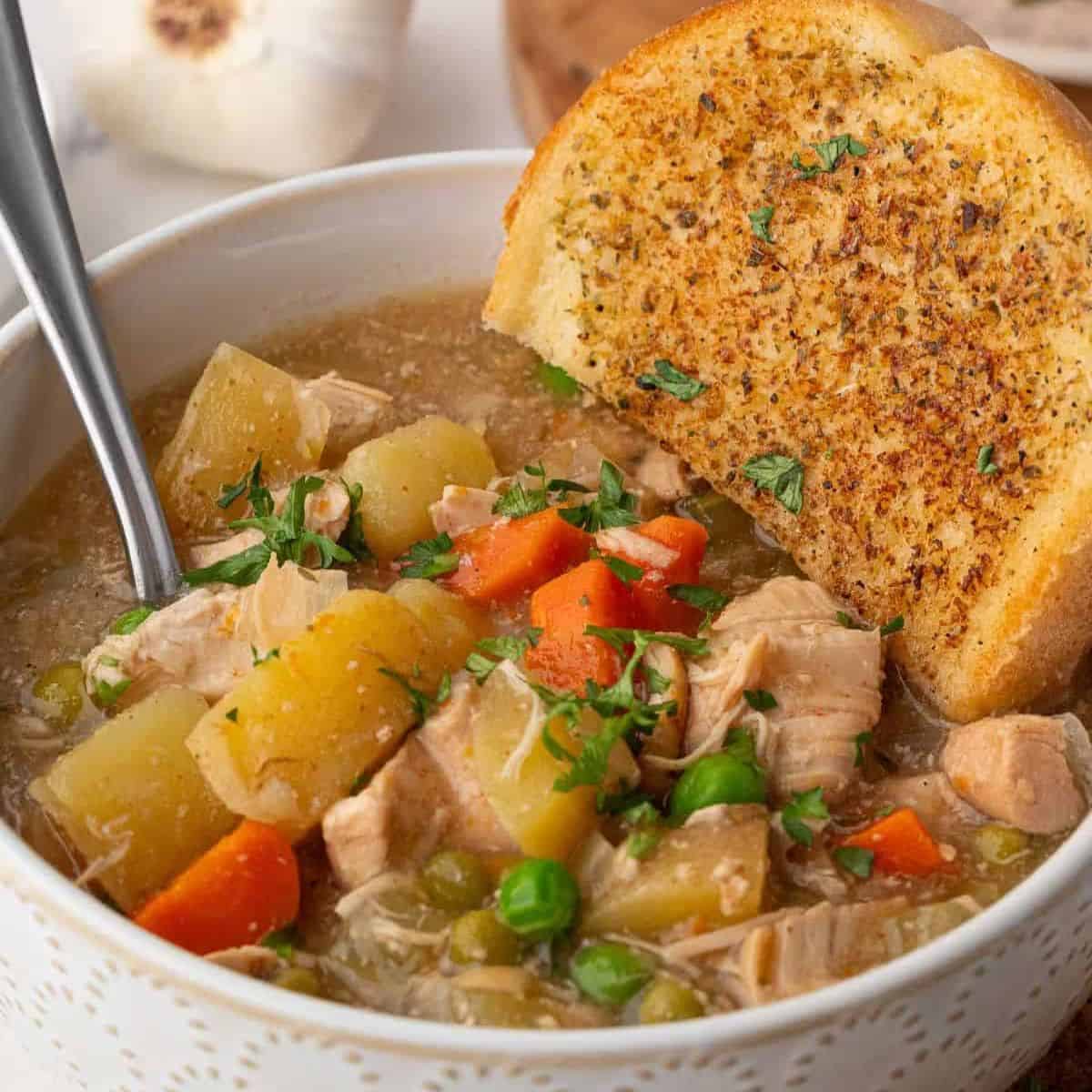 slow cooker chicken stew in a bowl with a spoon and garlic bread