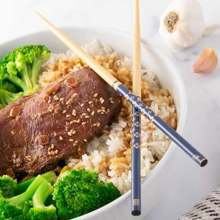 slow cooker honey garlic chicken in a bowl of rice and broccoli with chopsticks