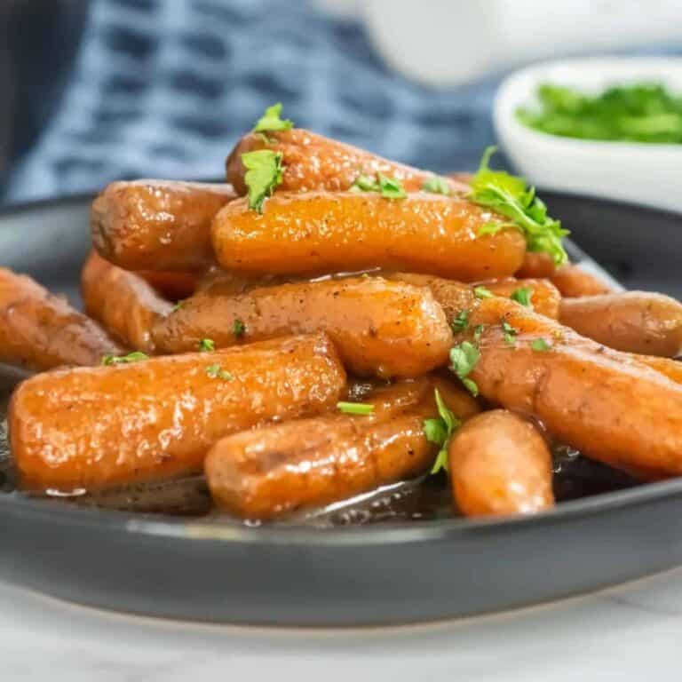 slow cooker glazed carrots sitting on a black plate with parsley on top