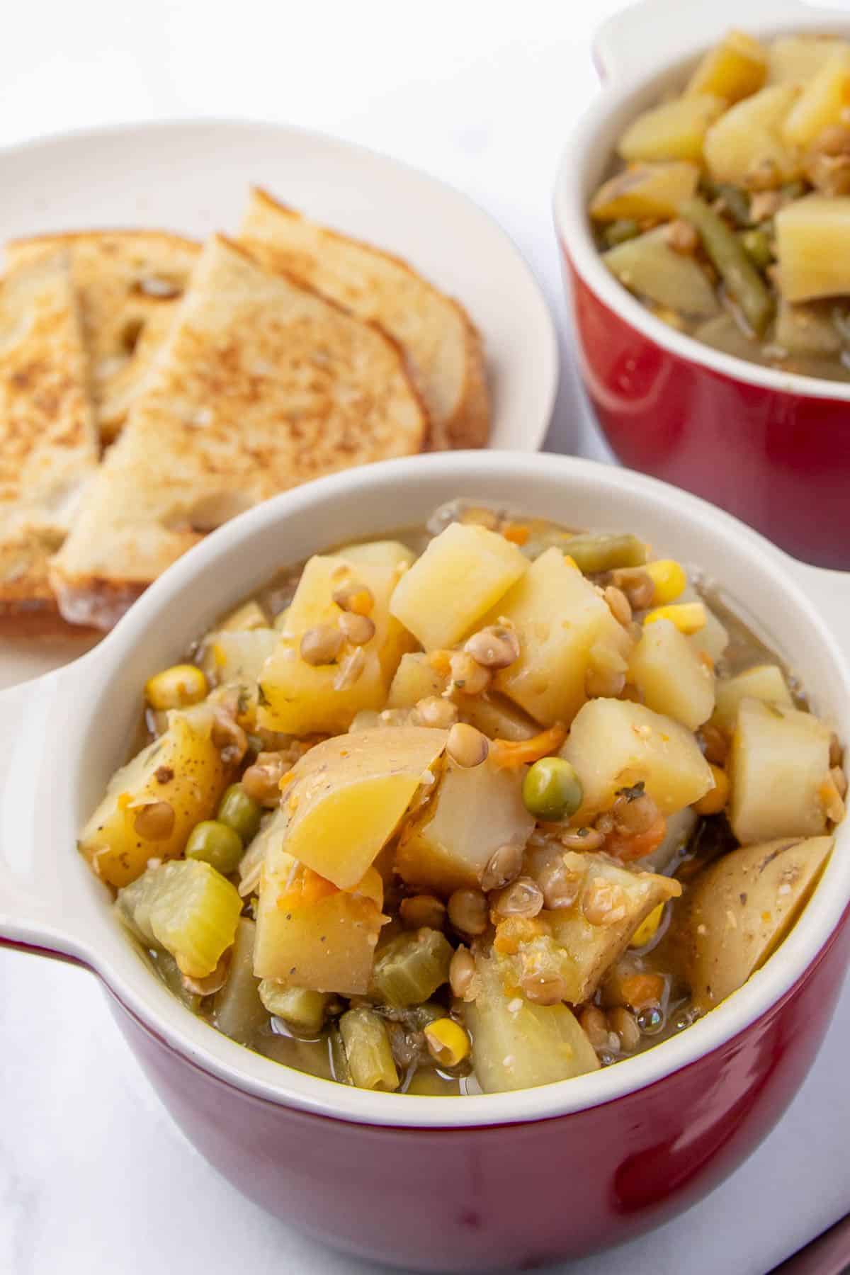 lose-up shots of the finished lentil stew served in red bowls, showcasing a mix of cubed potatoes, lentils, green beans, peas, and celery.