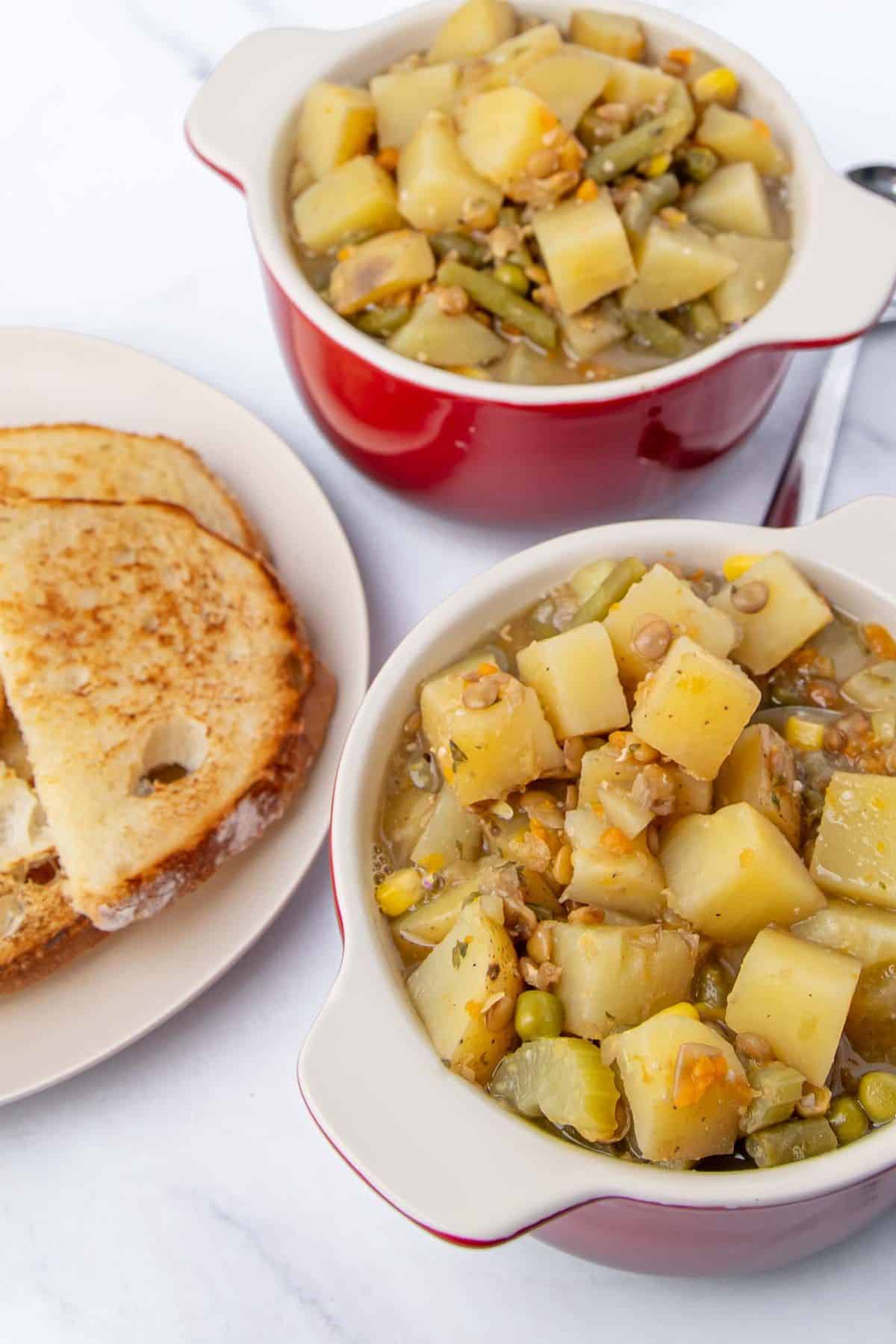 The stew is served in red bowls, showcasing chunky pieces of potatoes, lentils, and mixed vegetables like celery, and peas.