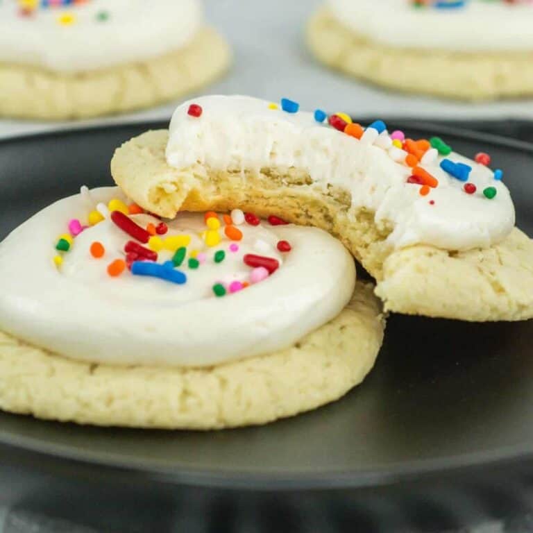 sour cream cookies with frosting on top and sprinkles sitting on a plate with one having a bite taken out