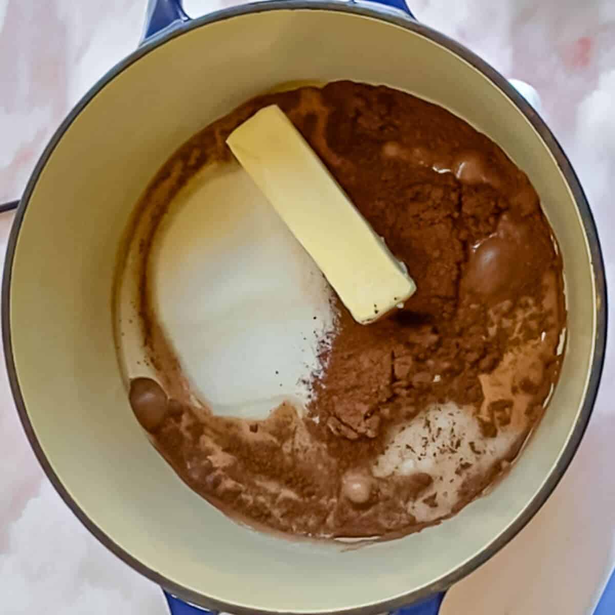 A pot with butter, sugar, cocoa powder, and milk, ready to be melted together.