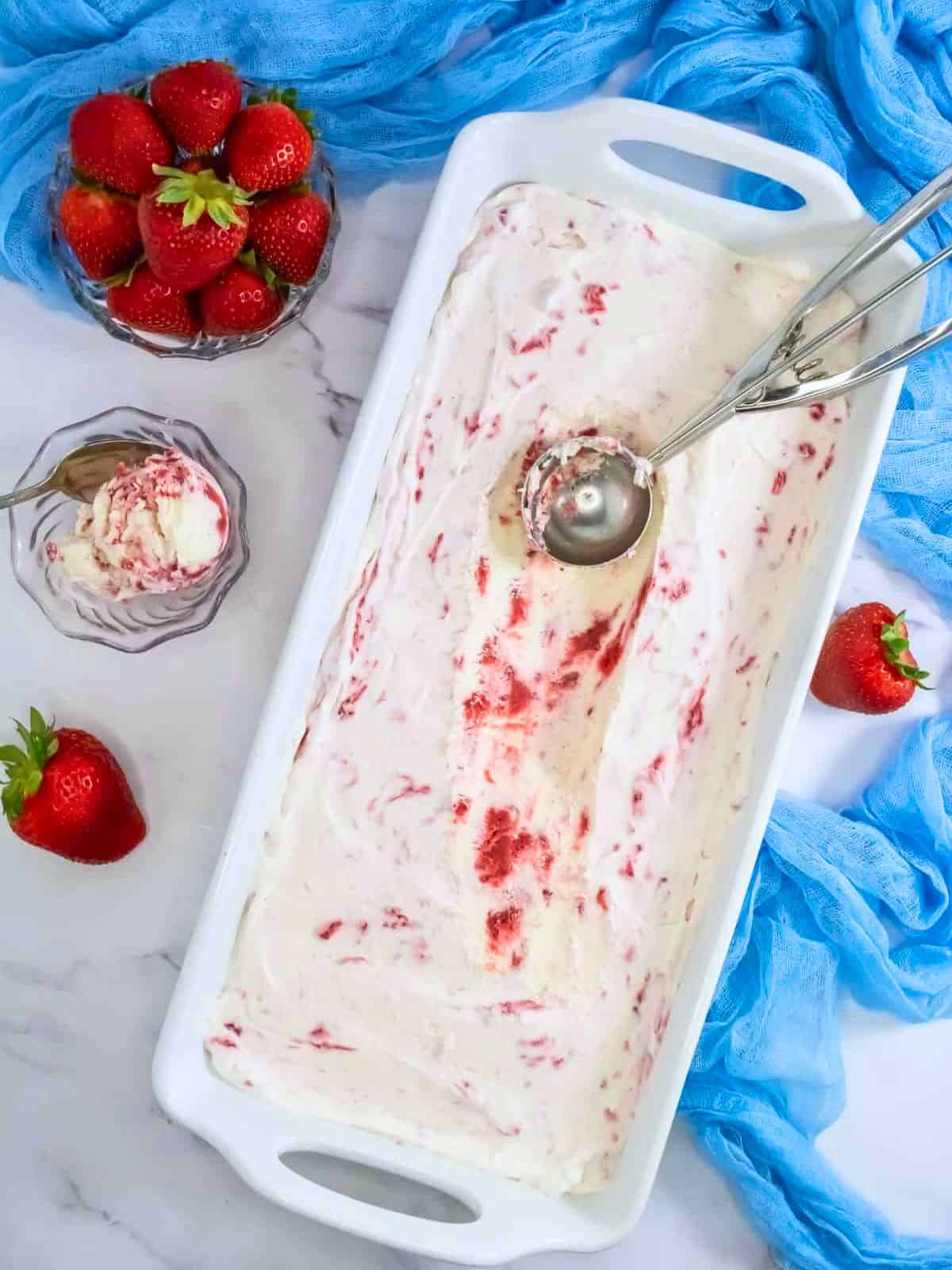 The final no-churn strawberry ice cream, partially scooped, with strawberries and ice cream served on the side.