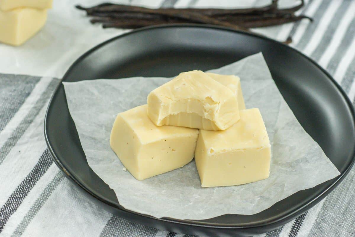 Vanilla fudge made with 3 ingredients on a piece of parchment paper on a black plate.