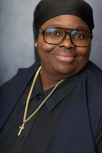 Professional religious leader wearing cross necklace and glasses, smiling confidently.
