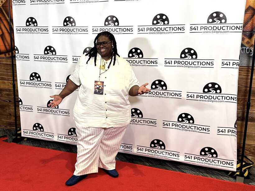 Beautiful woman standing on red carpet at 541 Productions event, smiling and posing, background with 541 Productions logo and event backdrop.