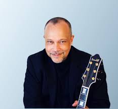 Close-up of a smiling man holding an electric guitar, portrait with a light blue background.