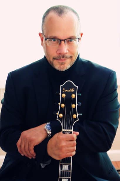 Elegant man in glasses holding an acoustic guitar, professional portrait for UOhnIt.com.